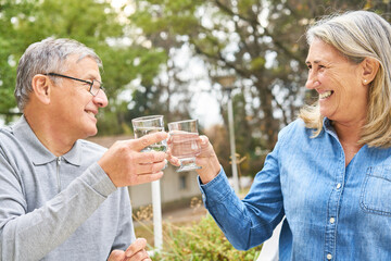 Cheerful elderly friends toasting glass of water in garden