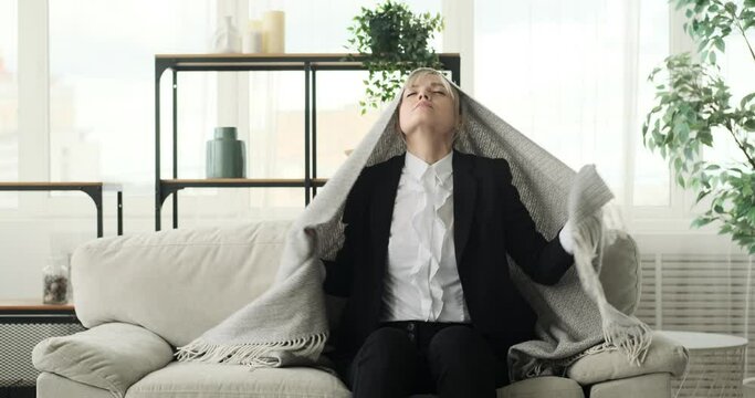 Businesswoman is seen taking a nap on the sofa, wrapped in a blanket. Her serene face and relaxed posture convey a sense of tranquility and rest. The reason could be tiredness from a busy workday.