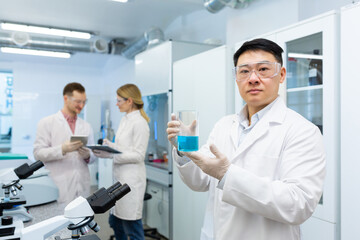 Portrait of an Asian medical scientist, man seriously thinking looking at the camera, laboratory technician working with a team of colleagues researchers.