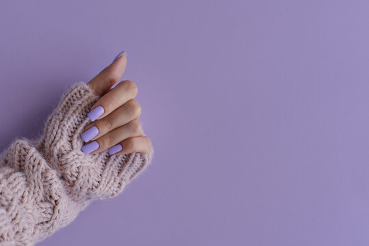 Female's hand with gelish manicure. Nails of trendy lavender color on purple background, copy space