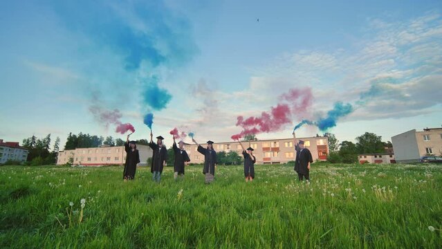 Graduates in costume walk with a smoky multi-colored smoke at sunset.