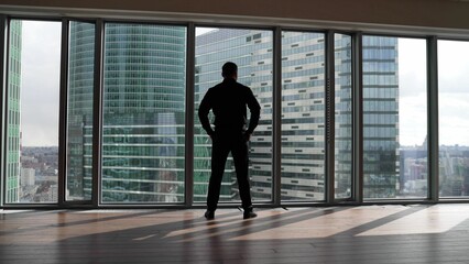 Fototapeta premium A man in a suit in the office opposite a panoramic window. A confident man approaches the window against the backdrop of skyscrapers.