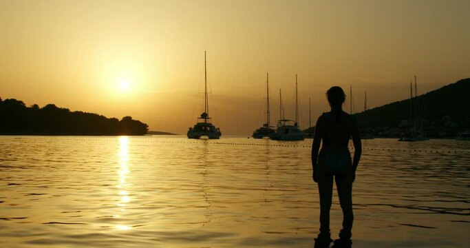 A young woman is standing in a shallow water, looking at the sunset on the Adriatic Sea in Croatia.