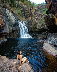 girl in bikini swimming in a rock pool under large tropical waterfall - jourama falls in paluma range national park near townsville, tropical north queensland, australia