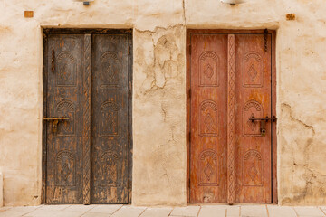 Old historic district in Dubai. Two ancient arabic wooden front doors with oriental pattern. Door surrounded by a clay wall.