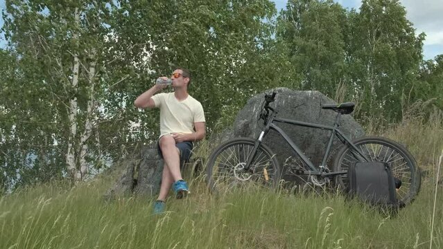 a cyclist stopped to rest and drinks water from a bottle in the woods