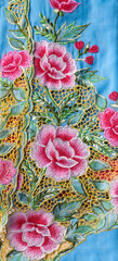 Blue kebaya cloth with intricate embroidery of pink flowers.