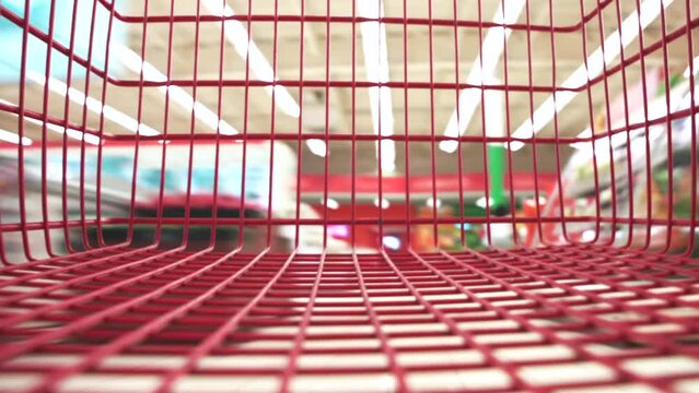 Timelapse close up view from the moving empty red shopping cart in a big grocery store. Fast motion around the supermarket with blurred background.