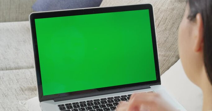 녹색 목업 화면이 떠 있는 노트북으로 업무를 하는 여성을 어깨 너머로 본 영상