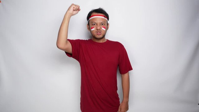 Excited Asian man wearing a red top and headband, showing strong gesture by lifting his arms and muscles smiling proudly. Indonesia's independence day concept.
