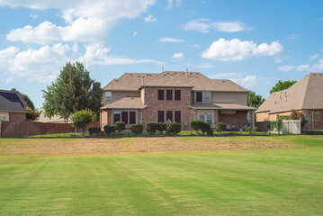 Large grassy and rolling lawn of suburban park next to upscale residential neighborhood row of two-story houses in Flower Mound, Texas, USA