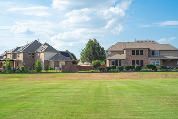Obraz premium Backyard view of two-story suburban houses with solar roof panels, metal fence near large rolling hill grassy lawn of suburban park Flower Mound, Texas, USA