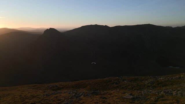 A paraglider floating through the sky in the mountains at sunrise
