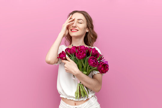 young cute girl in festive clothes holds bouquet of flowers and smiles on pink isolated background