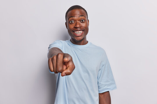 Enthusiastic cheerful African man dressed in casual tshirt pointing directly at camera with excitement smiles broadly dressed in casual blue t shirt isolated over white background. I choose ypu