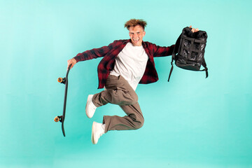 young guy student with backpack jumps and flies to school on skateboard on blue isolated background