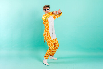 young funny guy in orange giraffe pajamas dances at party in sunglasses on blue isolated background