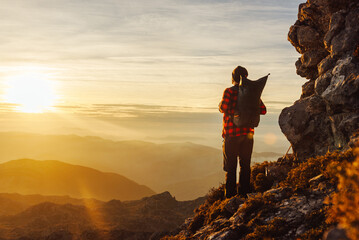 mountaineer on his back, unrecognizable, with a backpack, contemplating the sunset on the peak of a...