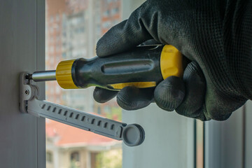 Male using screwdriver tightens screw that fixes plastic window opening limiter Close-up of gloved...