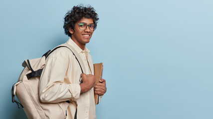 Sideways shot of cheerful male student with notepads and backpack ready for studying dressed...