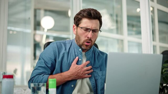 Closeup of working bearded man in glasses, difficulty breathing or chest pain, touches his chest with hand. Heart attack, thoracic osteochondrosis, panic attack concept. Trouble breathing, chest pain.