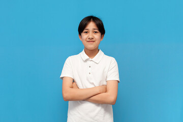 asian boy of twelve years old in white t-shirt stands with his arms crossed on blue isolated background, korean child