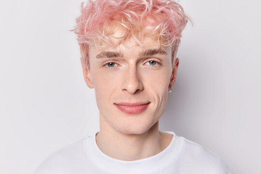 Portrait of handsome young pink haired man dressed in casual clothes smiles gladfully concentrated into camera expresses positive emotions isolated on white background. People and emtions concept