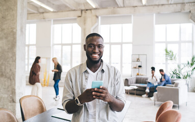 Cheerful ethnic man with smartphone in office