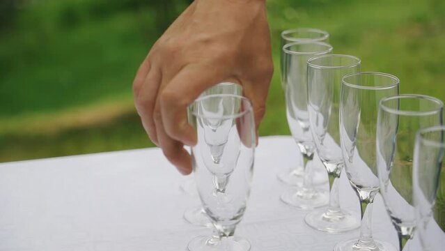 A man places glasses on a white tablecloth on the table. Shooting close-up in slow motion