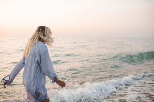 Attractive sensual woman wearing wet shirt running at beach over sea waves outdoors. Summer vacation season.