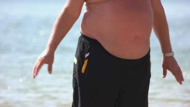 Mature man with belly fat standing on the beach. Obese and unhealthy lifestyle concept.