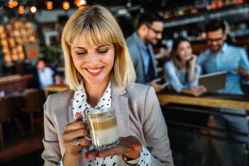 Portrait of happy young business woman drinking coffee in a break. In the background, her colleagues