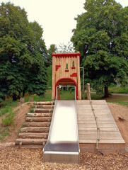 Spielgerät auf Spielplatz aus Holz mit Holzhaus und Rutsche in einem Park in grüner Natur. 