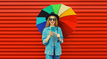 Obraz na płótnie Canvas Portrait of happy smiling young woman looking at phone with colorful umbrella on red background