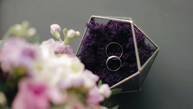 Shooting wedding rings in a jewelry box next to a bouquet of flowers on the table. Shooting from above