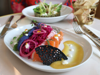 A plate of salmon gravlax or graved salmon with mixed colorful vegetables: radish, beetroot, sweet purple potatoes. It's a Nordic dish consisting of cured salmon using a mix of salt, sugar