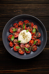 Burrata with baked cherry tomatoes and spices, on a plate, on a dark wooden background
