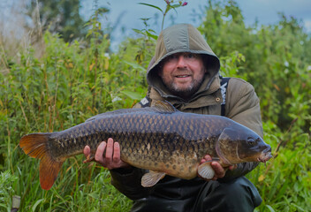 Fisherman holding up a common carp that he has caught with a smile on his face.