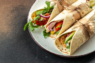 Burritos wraps with chicken, avocado, fresh tomatoes, limes on plate. Mexican dish. place for text, top view