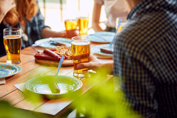 Young people, friends meeting together on warm day, sitting in pub, drinking delicious lager beer and having pleasant time together. Concept of oktoberfest, traditional taste, leisure time, enjoyment