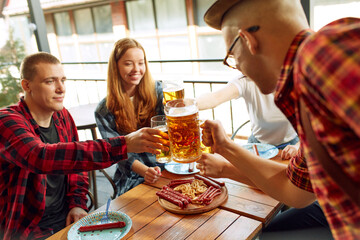 Young positive people, friends meeting st pub, cheerfully talking, drinking beer. Having food relaxed time together. Concept of oktoberfest, traditional taste, friendship, leisure time, enjoyment