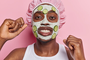 Horizontal shot of dark skinned young man cleans teeth with dental floss applies facial clay mask...