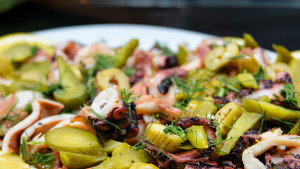 Boiled octopus salad is served with pure olive oil, lemon slices, dill, green olives and pickled...