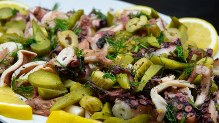 Boiled octopus salad is served with pure olive oil, lemon slices, dill, green olives and pickled cucumbers.  fresh and healthy seafood salad. Mediterranean gourmet appetizer.