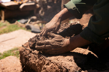 Man building with his hands an adobe house with adobe bricks and mud. Llachon region of Lake Titicaca in Peru.