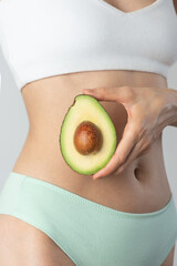 Avocado in female hands on the background of the body. Women's health, fertility, diet.