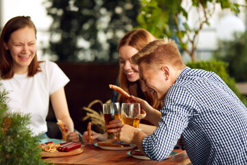 Young people, friends, couple sitting on open air restaurant, cafe pub, drinking beer, talking, having fun together. Concept of oktoberfest, traditional taste, friendship, leisure time, enjoyment