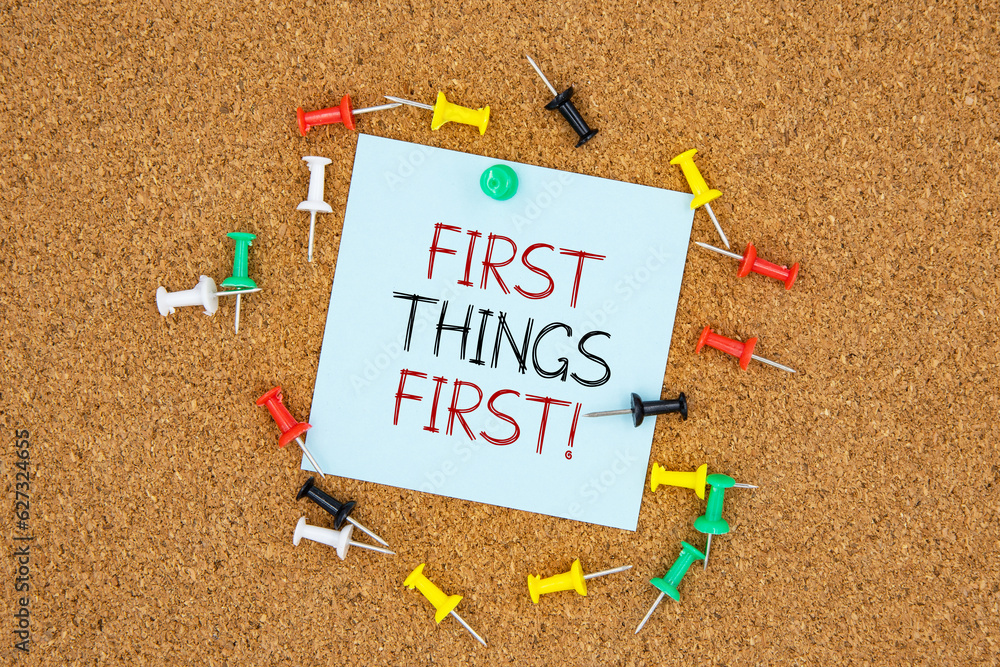Poster first things first text on light blue post-it paper pinned on bulletin cork board surrounding by mul