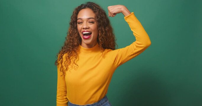 Powerful strong woman flexes arm muscle, winks smiles, greens studio background