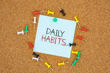 Daily habits text on light blue post-it paper pinned on bulletin cork board surrounding by multi...